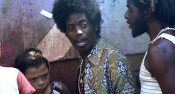 Movie still from “City of God” (2002), directed by Kátia Lund – A man in a colorful shirt is standing next to two other men; Close Up shot, Over the shoulder angle