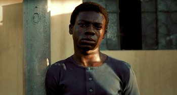 Movie still from “City of God” (2002), directed by Kátia Lund – A man with a black shirt is standing in front of a wall; Close Up shot, High angle