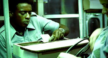 Movie still from “City of God” (2002), directed by Kátia Lund – A man sitting at a table cutting paper with a knife; Medium shot, Low angle