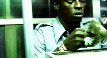 Movie still from “City of God” (2002), directed by Kátia Lund – A man sitting at a table looking at a book; Close Up shot, Low angle