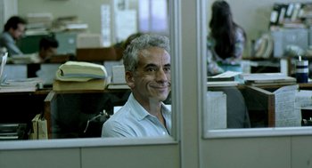 Movie still from “City of God” (2002), directed by Kátia Lund – A man sitting in an office cubicle looking out a window; Medium shot, Over the shoulder angle