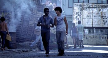 Movie still from “City of God” (2002), directed by Kátia Lund – Two young men walking down the street talking to each other; Wide shot, Low angle