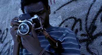Movie still from “City of God” (2002), directed by Kátia Lund – A man taking a picture with a camera; Close Up shot, Low angle