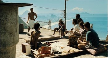 Movie still from “City of Men” (2007), directed by Paulo Morelli – A group of people sitting on the ground in front of a body of water; Wide shot, Low angle
