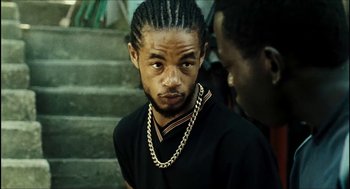 Movie still from “City of Men” (2007), directed by Paulo Morelli – A man with a beard and a chain around his neck is looking at the camera; Close Up shot, Low angle