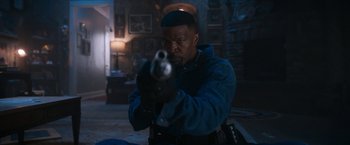 Movie still from “Day Shift” (2022), directed by J.J. Perry – A man holding a gun in a room with pictures on the walls; Medium shot, Over the shoulder angle