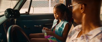 Movie still from “Day Shift” (2022), directed by J.J. Perry – A girl sitting in the back seat of a car looking at her cell phone; Medium shot, Over the shoulder angle