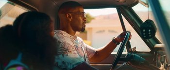 Movie still from “Day Shift” (2022), directed by J.J. Perry – A man driving a car in the sunlight; Medium shot, Over the shoulder angle