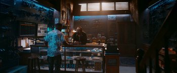 Movie still from “Day Shift” (2022), directed by J.J. Perry – A man standing at the counter of a gun shop; Wide shot, High angle