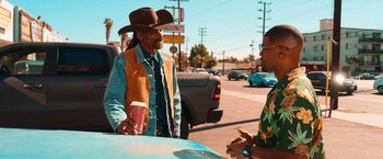Movie still from “Day Shift” (2022), directed by J.J. Perry – A man wearing a cowboy hat talks to a woman on the side of the road; Medium shot, Over the shoulder angle