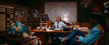 Movie still from “Day Shift” (2022), directed by J.J. Perry – A man sitting at a desk in front of a map of san fransisco; Wide shot, Over the shoulder angle