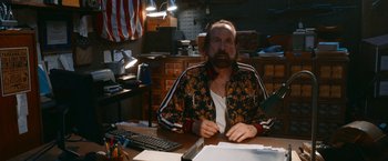 Movie still from “Day Shift” (2022), directed by J.J. Perry – A man sitting at a desk in front of a computer; Medium shot, Over the shoulder angle