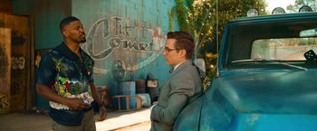 Movie still from “Day Shift” (2022), directed by J.J. Perry – A man standing next to a car in front of a building; Medium shot, Over the shoulder angle