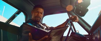 Movie still from “Day Shift” (2022), directed by J.J. Perry – A man sitting in a car reading a magazine; Close Up shot, Over the shoulder angle