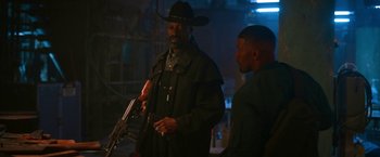 Movie still from “Day Shift” (2022), directed by J.J. Perry – A man in a cowboy hat holding a gun and talking to another man; Medium shot, Over the shoulder angle