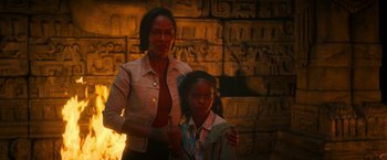 Movie still from “Day Shift” (2022), directed by J.J. Perry – A woman standing next to a young girl near a fire pit; Medium shot, High angle