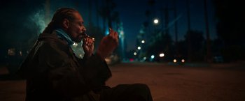 Movie still from “Day Shift” (2022), directed by J.J. Perry – A man sitting on the side of the road while smoking a cigarette; Medium shot, Low angle