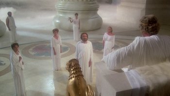 Movie still from “Clash of the Titans” (1981), directed by Desmond Davis – A group of people dressed in white standing in front of a statue; Wide shot, High angle