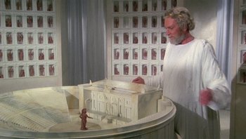 Movie still from “Clash of the Titans” (1981), directed by Desmond Davis – An older man looking at an architectural model; Wide shot, High angle