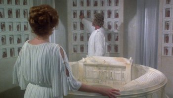 Movie still from “Clash of the Titans” (1981), directed by Desmond Davis – A man and a woman are looking at pictures on a wall; Medium shot, Over the shoulder angle