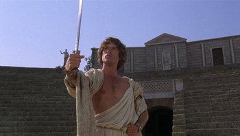 Movie still from “Clash of the Titans” (1981), directed by Desmond Davis – A man holding a sword while standing in front of a building; Medium shot, Low angle
