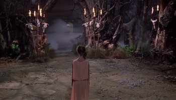 Movie still from “Clash of the Titans” (1981), directed by Desmond Davis – A girl in a pink dress stands in front of candles; Wide shot, High angle