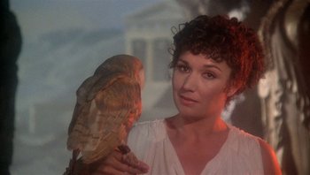 Movie still from “Clash of the Titans” (1981), directed by Desmond Davis – A woman holding an owl while standing next to a building; Close Up shot, Low angle