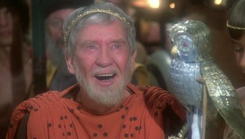 Movie still from “Clash of the Titans” (1981), directed by Desmond Davis – An old man with a beard wearing a crown and holding an owl; Close Up shot, Over the shoulder angle