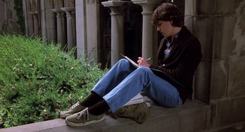Movie still from “Class” (1983), directed by Lewis John Carlino – A man sitting on a ledge writing on a piece of paper; Wide shot, High angle