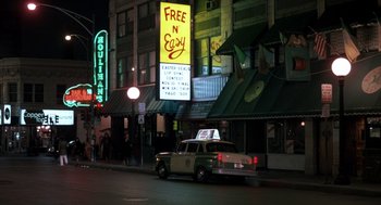 Movie still from “Class” (1983), directed by Lewis John Carlino – A car driving down a street next to a neon sign; Extreme Wide shot, High angle