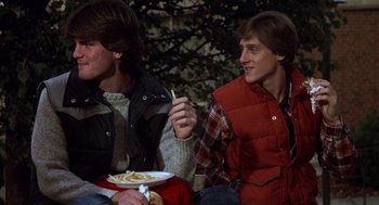 Movie still from “Class” (1983), directed by Lewis John Carlino – Two young men sitting next to each other eating food; Medium shot, Over the shoulder angle