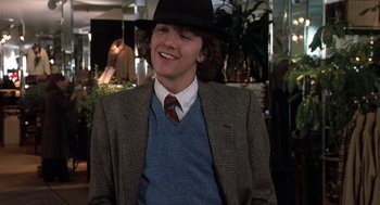 Movie still from “Class” (1983), directed by Lewis John Carlino – A young man in a suit and hat smiling for the camera; Medium shot, Over the shoulder angle