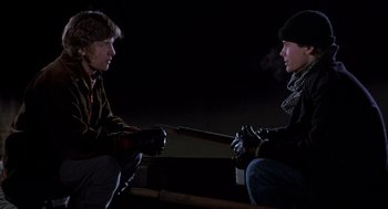 Movie still from “Class” (1983), directed by Lewis John Carlino – Two young men sitting in the dark with one holding a gun; Medium shot, Over the shoulder angle
