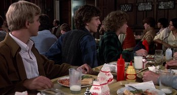 Movie still from “Class” (1983), directed by Lewis John Carlino – A group of people sitting at a table with food; Medium shot, Over the shoulder angle