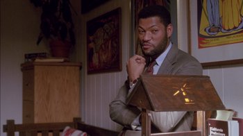 Movie still from “Class Action” (1991), directed by Michael Apted – A man in a suit and tie sitting at a table in a room; Medium shot, Low angle
