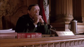 Movie still from “Class Action” (1991), directed by Michael Apted – A man sitting in front of a microphone in a courtroom; Medium shot, Low angle