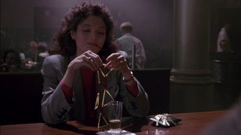 Movie still from “Class Action” (1991), directed by Michael Apted – A woman sitting at a table with a glass of wine and a stack of matches; Medium shot, Low angle
