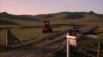 Movie still from “Class Action” (1991), directed by Michael Apted – A tractor is driving down a dirt road in the middle of a field; Extreme Wide shot, High angle