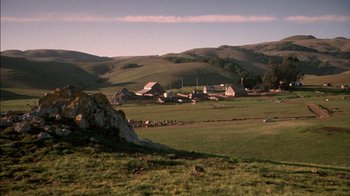 Movie still from “Class Action” (1991), directed by Michael Apted – A green field with a few buildings in the background; Extreme Wide shot, High angle