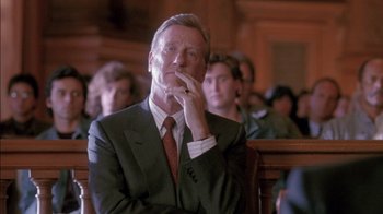 Movie still from “Class Action” (1991), directed by Michael Apted – A man in a suit and tie sitting in front of a group of people; Close Up shot, Low angle