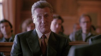 Movie still from “Class Action” (1991), directed by Michael Apted – An older man wearing a suit and tie in front of a group of people; Close Up shot, Over the shoulder angle