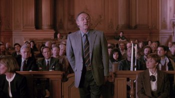 Movie still from “Class Action” (1991), directed by Michael Apted – A man standing in front of a group of people in a courtroom; Medium shot, Low angle