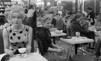 Movie still from “Cléo from 5 to 7” (1962), directed by Agnès Varda – A group of people sitting at tables in a room; Medium shot, Over the shoulder angle
