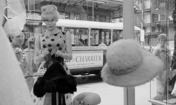 Movie still from “Cléo from 5 to 7” (1962), directed by Agnès Varda – A woman standing in front of a bus and looking at a hat; Medium shot, Low angle