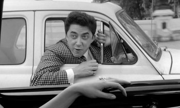 Movie still from “Cléo from 5 to 7” (1962), directed by Agnès Varda – A black and white photo of a man and a woman in the driver's seat of a car; Medium shot, Low angle