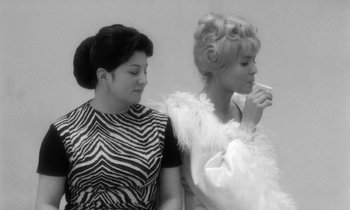 Movie still from “Cléo from 5 to 7” (1962), directed by Agnès Varda – Two women standing next to each other and one of the women is holding a cigarette; Medium shot, Low angle