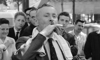 Movie still from “Cléo from 5 to 7” (1962), directed by Agnès Varda – An older man is eating something while standing in front of a group of men; Close Up shot, Low angle