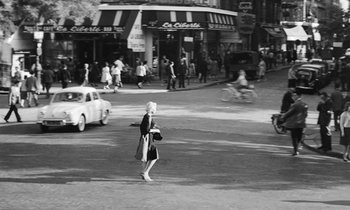Movie still from “Cléo from 5 to 7” (1962), directed by Agnès Varda – A woman walking down a street holding a bag; Extreme Wide shot, High angle
