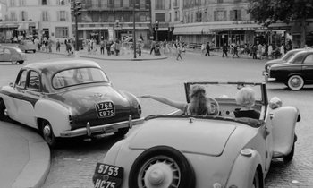 Movie still from “Cléo from 5 to 7” (1962), directed by Agnès Varda – An old photo of a woman driving a car on the street; Wide shot, High angle