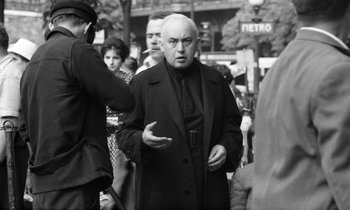 Movie still from “Cléo from 5 to 7” (1962), directed by Agnès Varda – An older man is talking to a group of people; Medium shot, Over the shoulder angle